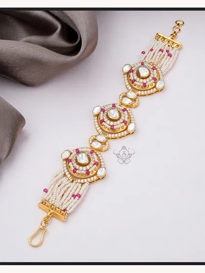 A traditional yet stylish bracelet made with multiple strands of pearls and ornate polki diamond motifs accented with rubies. This piece is perfect for weddings and festive occasions.