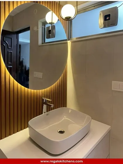 A compact and stylish vanity solution. The combination of a rectangular vessel sink and a round, backlit mirror against a fluted wood panel creates a chic focal point.