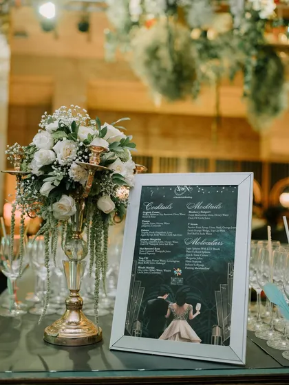 The bar setup, complete with a custom-designed menu that matches the event's elegant, art-deco-inspired aesthetic, and a classic white rose centerpiece.