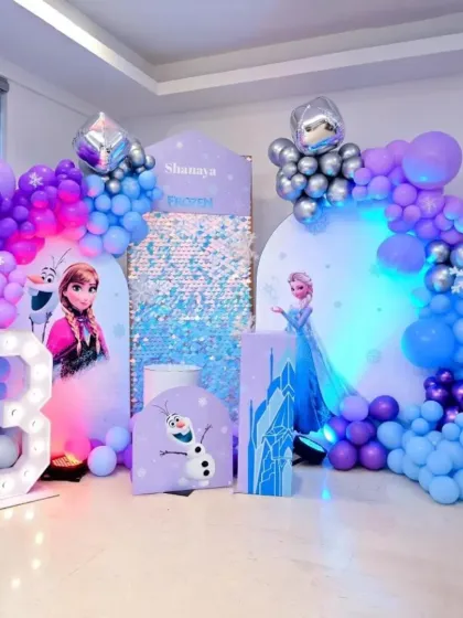 Let it go! This Frozen-themed party for Shanaya's 3rd birthday brings the magic of Arendelle to life. It features life-sized cutouts of Anna and Elsa, a sparkling shimmer backdrop, and a cool blue and purple balloon arch, creating a winter wonderland.