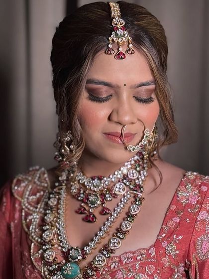 This bride is adorned in a magnificent, heavily layered bridal set. The combination of multiple necklaces, a statement maang tikka, and a detailed nath creates a look of unparalleled grandeur.