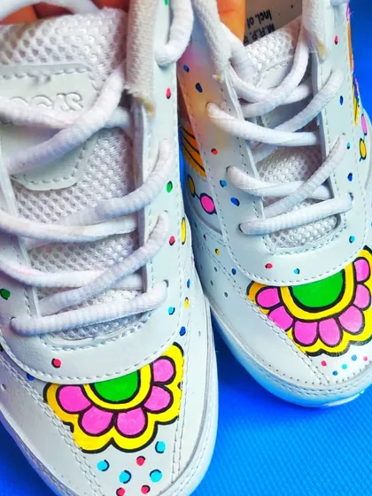 A front view of the sneakers, highlighting the symmetrical floral design on the toe box, complemented by colorful dots.