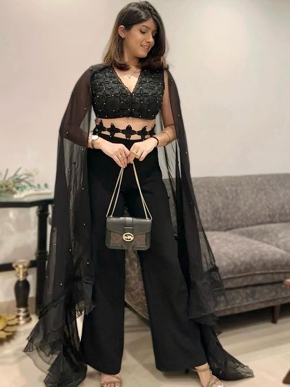 The full view of this black party outfit. Paired with a simple black bag, the focus remains on the unique silhouette of the crop top and cape.