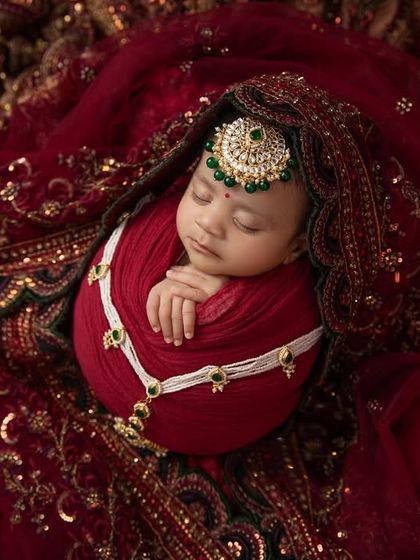 A close up of this precious baby, showcasing the delicate jewelry and the luxurious red and gold fabric that envelops her. This is a modern heirloom in the making.
