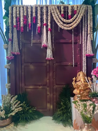 A traditional door is framed with garlands of jasmine and pink flowers. This simple yet beautiful entrance decor is perfect for an intimate engagement or home ceremony.