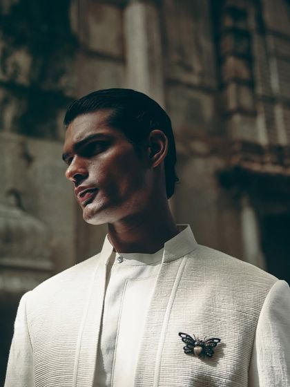A strong profile shot highlighting the sharp cut of the jacket and the subtle insect brooch, a key styling detail for this Dhruv Vaish look.