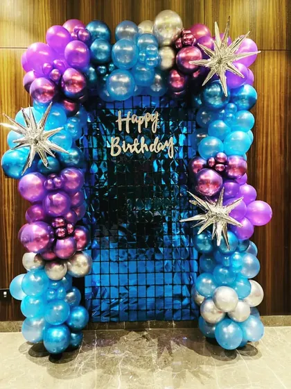 A stunning balloon arch in metallic shades of blue, purple, and silver. This decoration frames a blue sequin backdrop, perfect for a glamorous birthday photo op.