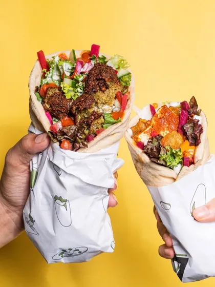 Held up against a bright yellow background, these falafel wraps look fresh, vibrant, and ready to eat. This style of lifestyle shot is effective for showing off grab-and-go food items in an appetizing way.