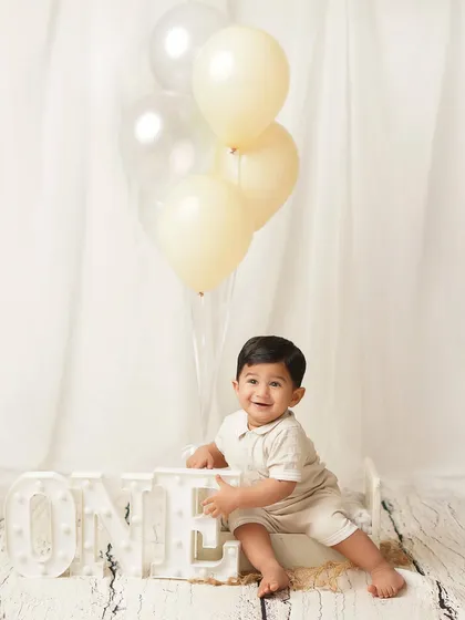 A perfect first birthday portrait, with the little boy smiling proudly next to his 'ONE' sign and balloons. A classic memory to cherish.