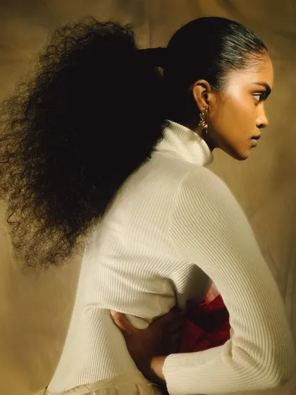 A profile shot of 'ANAINA,' showcasing her voluminous ponytail. The soft lighting and neutral background create a timeless and elegant portrait.