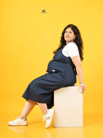 A modern and casual solo maternity portrait. The denim overalls and bright yellow background create a fun, fresh, and youthful vibe.