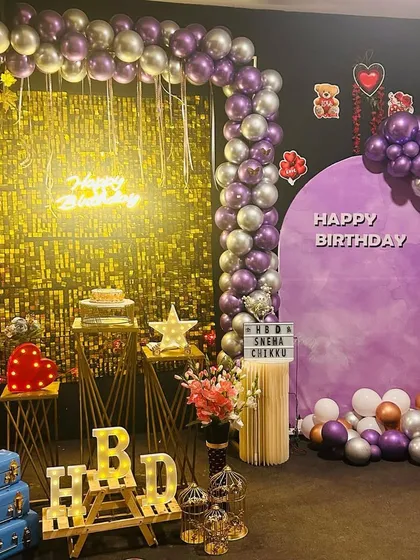 I love creating the perfect backdrop for your photos. This setup with a shimmery gold wall, purple and silver balloons, and a neon 'Happy Birthday' sign is just one of the many themes we can create for your special day.