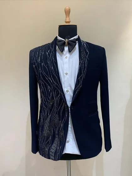 A navy blue tuxedo on a mannequin, featuring abstract silver and gold embroidery on one side. This asymmetrical design is modern and artistic.