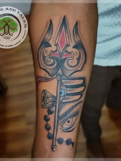 A powerful Trishul tattoo on the forearm, combined with a Rudraksha and the third eye of Lord Shiva. The red accent on the Trishul adds a focal point to the black and grey design.