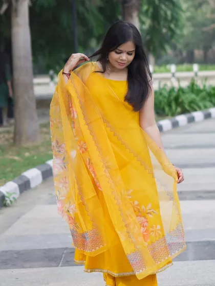 A candid-style photo from the yellow suit series. The model is adjusting her hair, creating a natural and relatable fashion moment.