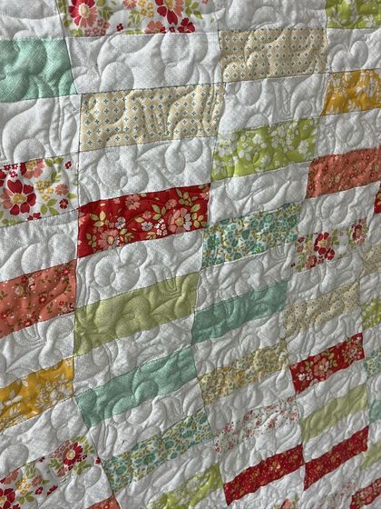 A close-up of the hand-pieced quilt, showing the gentle, curving quilting pattern.
