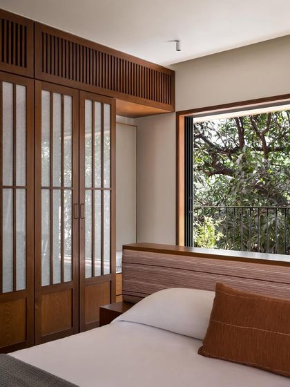 A full view of the master bedroom's custom island bed and headboard. The low height of the headboard ensures the view of the trees outside remains the main event.