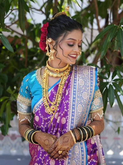 This bride looks stunning in a traditional Maharashtrian gold-finish jewellery set, perfectly complementing her purple and blue nauvari saree.