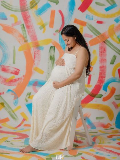 A serene solo portrait of the mother-to-be, her white dress contrasting beautifully with the vibrant, artistic background.