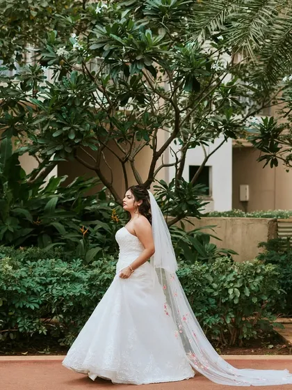 A graceful walk in the garden. The long, flowing veil with floral details adds a touch of romance to her classic bridal look.