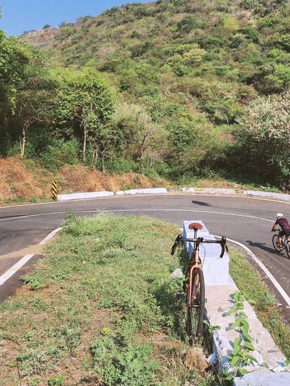A cyclist tackles a hairpin bend on a quiet road, while another bike waits, ready for the next leg of the journey. This shot highlights both the challenge and the beauty of our curated mountain routes.