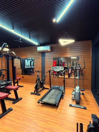 A closer look at the cardio section, featuring a treadmill, stationary bike, and cross-trainer. The wood-paneled accent wall adds warmth to the design, contrasting with the dark ceiling and walls for a balanced, modern aesthetic.