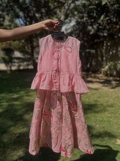 This pink lehenga set features a peplum top with ruffles and a printed skirt with bird motifs. It’s a perfect blend of modern style and traditional charm, designed for comfort and play.