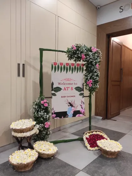 A traditional and elegant baby shower entrance, featuring a bamboo frame adorned with fresh pink roses and baskets of white flowers.