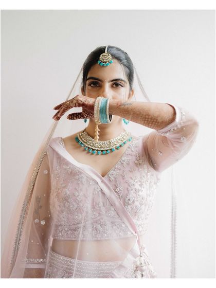 A striking bridal portrait of Karishma. The way she uses her hand and the veil to partially cover her face creates a sense of mystery and highlights her expressive eyes.