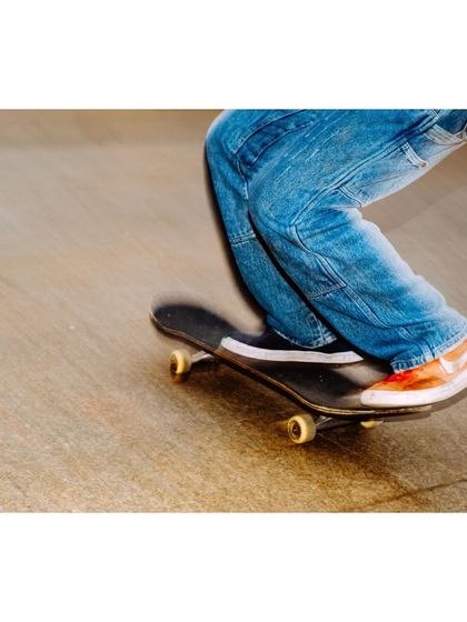 A panning shot focusing on the lower half of a skater, capturing the motion of the skateboard. The blur effect emphasizes speed and the urban energy of skateboarding.