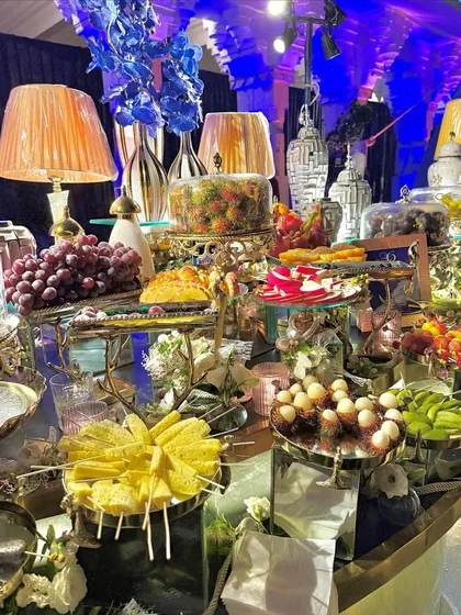 A lavish grazing table featuring an abundance of desserts and fresh fruits. This stunning display includes cakes, pastries, fruit skewers, and exotic fruits like rambutan and dragon fruit.