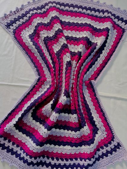 The beautiful wave effect created by this striped blanket in shades of purple and pink. The pattern is a simple variation of the granny stitch, creating a modern and eye-catching design.