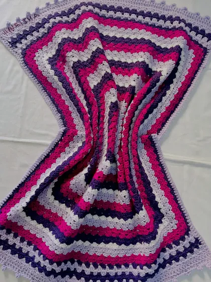 The beautiful wave effect created by this striped blanket in shades of purple and pink. The pattern is a simple variation of the granny stitch, creating a modern and eye-catching design.