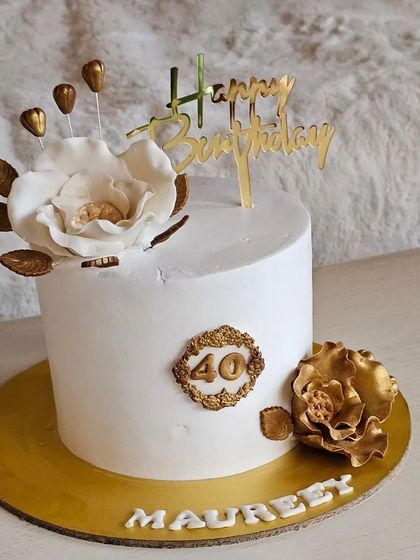 A sophisticated 40th birthday cake in white and gold, featuring a large white sugar flower and delicate gold accents.