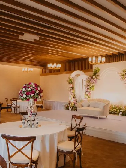 A wide view of an elegant engagement party setup, showing the beautiful floral stage, classic round tables with white linens, and warm, inviting lighting.