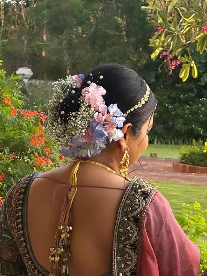A breathtaking view of a bridal bun with a mix of pastel pink and blue flowers against a lush green backdrop. This style is perfect for a destination wedding, adding a touch of nature's beauty to the bridal look.