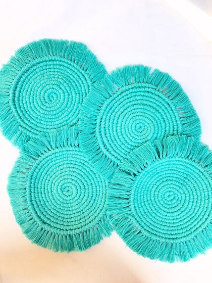 A set of four round macrame coasters in a beautiful turquoise color. These feature a classic spiral design with a short fringe, perfect for everyday use and adding a subtle bohemian touch to your coffee table.