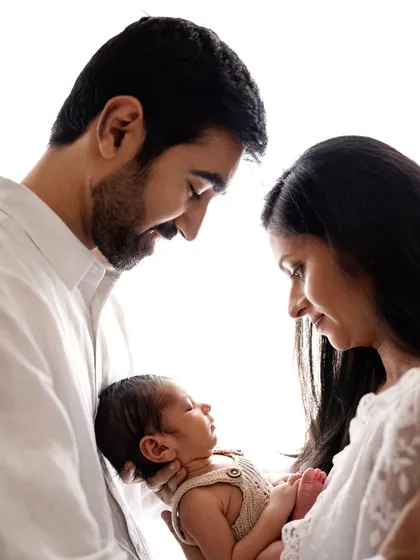 A classic and beautiful portrait of new parents gazing lovingly at their baby. The high-key white background keeps the focus entirely on them.