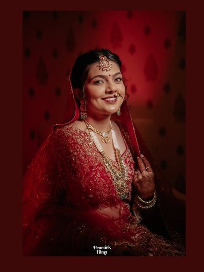 A warm, glowing portrait of the bride in her red wedding lehenga. Her happy smile captures the joy and excitement of her special day.