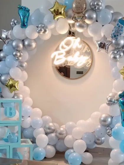 An elegant and modern 'Oh Baby' setup, perfect for a baby shower or welcome home party for a boy. This design is built around a full circular balloon arch in pastel blue, white, and chrome silver, with a central neon sign. I also include themed props like 'BABY' display boxes and foil balloons shaped like baby bottles.