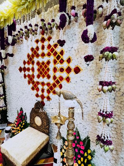 A backdrop made entirely of white flowers, featuring a geometric pattern in red. Hanging garlands with lotus buds add an extra layer of detail.