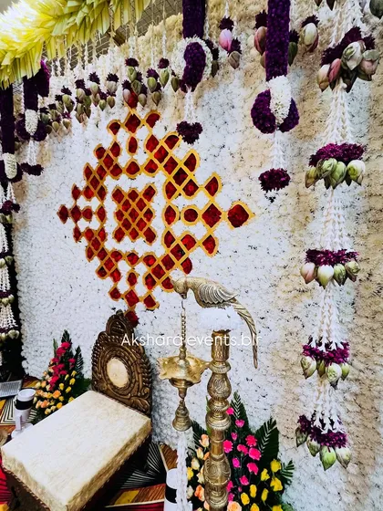 A backdrop made entirely of white flowers, featuring a geometric pattern in red. Hanging garlands with lotus buds add an extra layer of detail.