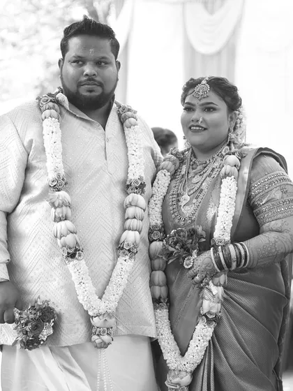 A classic black and white portrait of the wedding couple, showcasing their traditional attire and garlands.