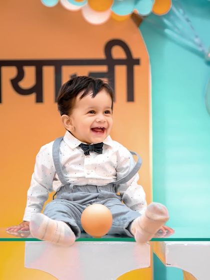 A moment of pure joy from a first birthday photoshoot. Dressed in a smart outfit with a bow tie, the birthday boy's laughter is contagious as he plays in his custom-decorated party space.