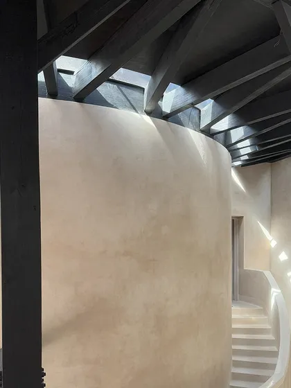 Long, curvilinear skylights and charred timber rafters create a dance of light and shadow across the lime-washed walls of the House of Galleries. The contrast between the dark wood and the light plaster is a key design feature.
