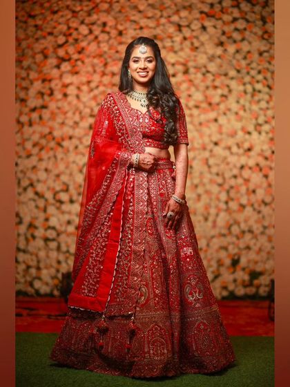 A full-length portrait of the bride in her red reception lehenga, looking regal and happy.