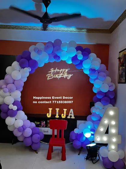 A purple and white balloon ring for a 4th birthday party at home. The decor includes a neon sign, light-up name, and a marquee number '4'.