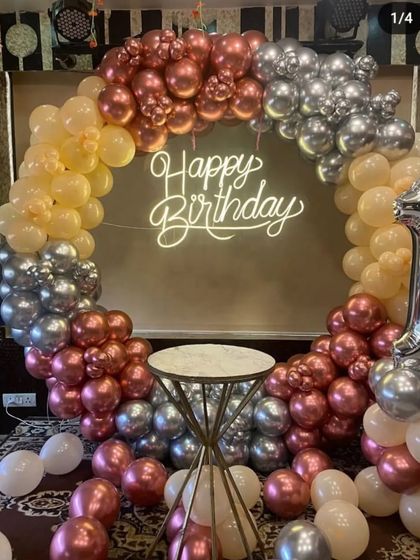 A stylish birthday balloon ring using a mix of rose gold, peach, and silver chrome balloons, with a central pedestal for the cake.