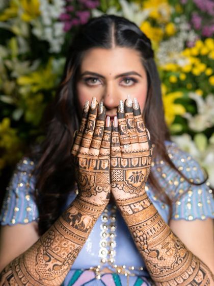 A confident and beautiful bride, with her hands framing her face to show off the intricate details of her bridal mehendi.