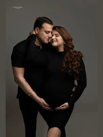 An intimate portrait of togetherness. Dressed in matching black, this couple shares a quiet, loving moment, their hands gently cradling the baby bump.